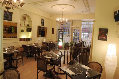 La salle du restaurant : tables dressées sous un lustre, grandes fenêtres donnant sur la rue