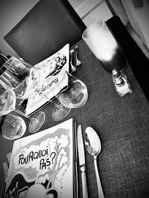 Photo en noir et blanc : la carte du restaurant posée sur une table dressée, verres au premier plan