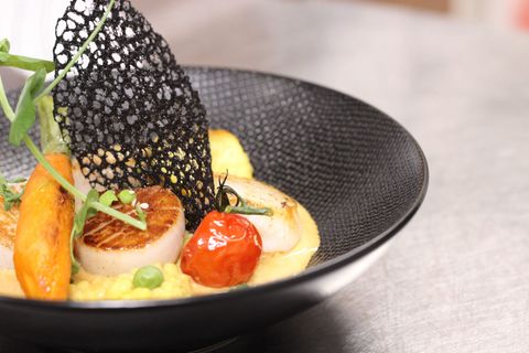 Scallops with a lace tuile served in a black textured bowl
