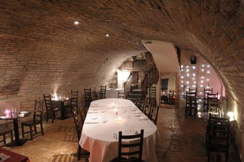 La cave voûtée dressée pour un banquet : longue table en nappe blanche sous la voûte en pierre